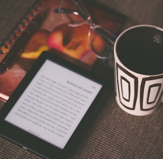 black E-book reader beside white and black mug