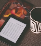 black E-book reader beside white and black mug