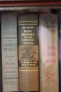 A row of vintage hardcover books with visible spines. Titles include 'Yankee Priest' by Edward F. Murphy, 'Basic History of the United States' by Charles A. and Mary R. Beard, and 'Three Detective Novels' by John Dickson Carr. The books are neatly arranged and display a variety of muted colors and classic typography.