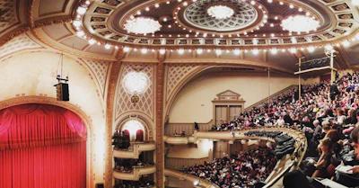 Audience applauding in an elegant opera house filled with warm lighting.