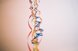 Colorful ribbons hang vertically against a plain background. The ribbons include shades of blue, red, yellow, and orange, creating a festive and decorative appearance.