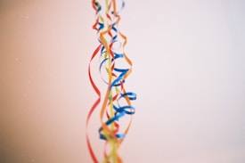 Colorful ribbons hang vertically against a plain background. The ribbons include shades of blue, red, yellow, and orange, creating a festive and decorative appearance.
