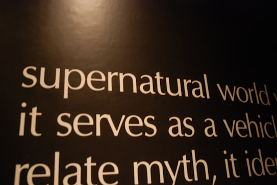 Text in white font is displayed on a dark background. The words include 'supernatural world', 'it serves as a vehicle', and 'relate myth'. The lighting casts a warm tone across the image, giving the text an expressive look.