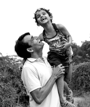 A father playing and laughing with his child in a park setting.