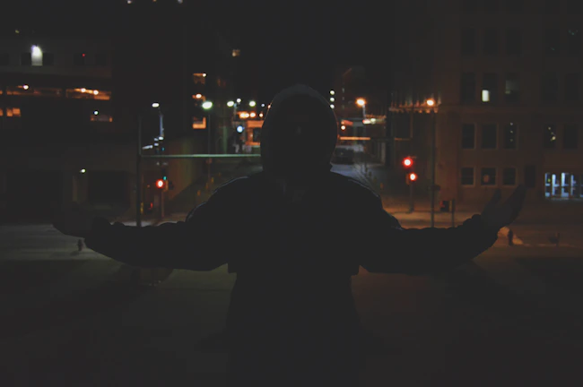 Nighttime cityscape with a silhouette wearing a nevrsettlin hoodie under streetlights.