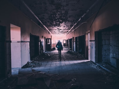 A shadowy figure exploring an abandoned building at dusk with a flashlight.