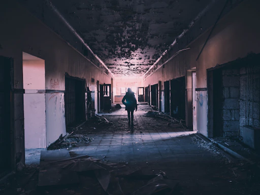 A shadowy figure holding a lantern in a foggy, abandoned house corridor.