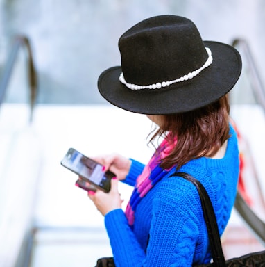 woman in blue and orange long sleeve shirt wearing black hat holding black smartphone