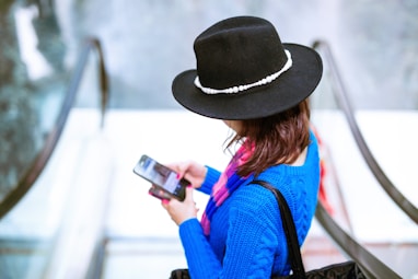 woman in blue and orange long sleeve shirt wearing black hat holding black smartphone