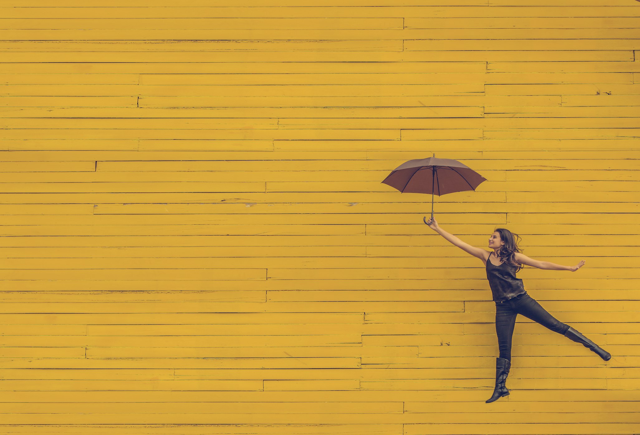 Happy girl jumping in front of yellow wall holding umbrella