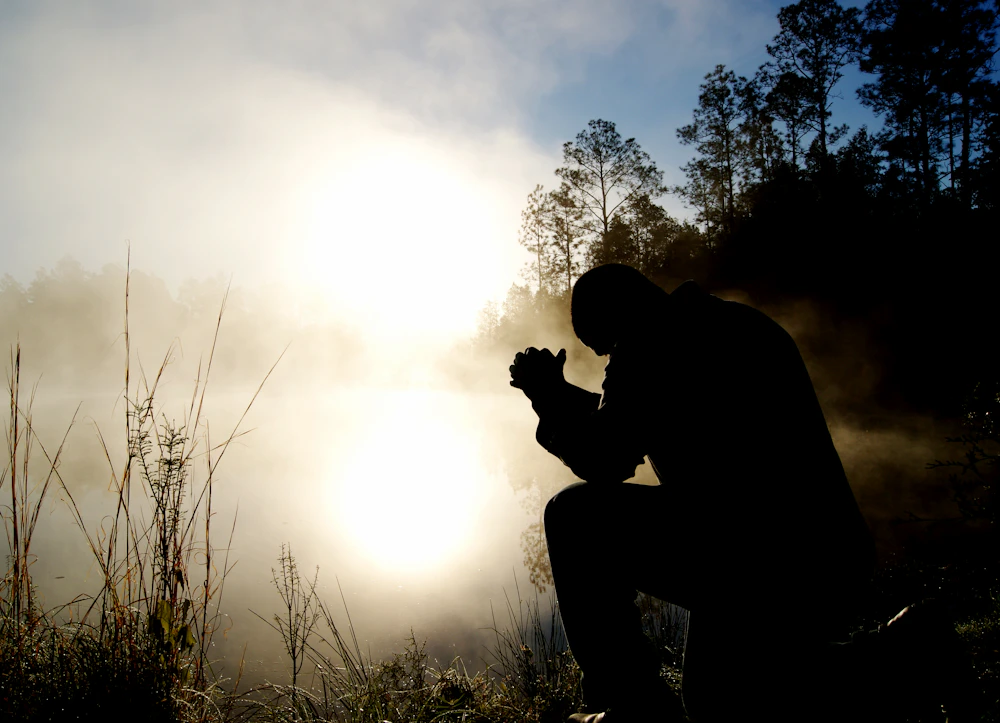 A silhouette of a person kneeling in prayer against warm golden light