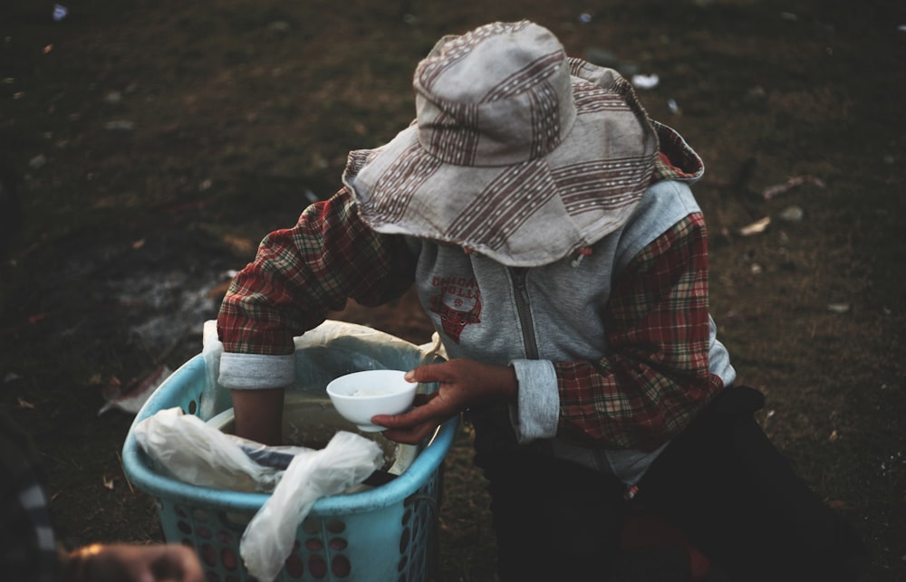 person in hat holding bowl while hand inside basket