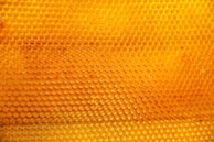 A close-up view of a honeycomb structure made of numerous hexagonal cells, varying in shades of yellow to orange, conveying a sense of natural organization and symmetry.