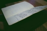 A notebook is open on a table, displaying pages filled with handwritten notes. The environment is softly lit, emphasizing the written content and creating a focused atmosphere.