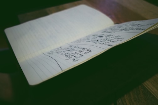 A notebook is open on a table, displaying pages filled with handwritten notes. The environment is softly lit, emphasizing the written content and creating a focused atmosphere.