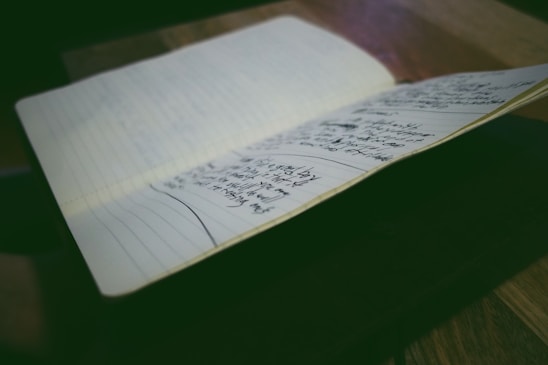 A notebook is open on a table, displaying pages filled with handwritten notes. The environment is softly lit, emphasizing the written content and creating a focused atmosphere.