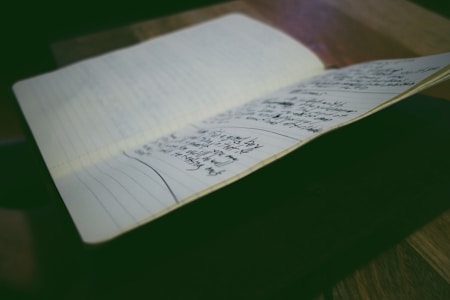 A notebook is open on a table, displaying pages filled with handwritten notes. The environment is softly lit, emphasizing the written content and creating a focused atmosphere.