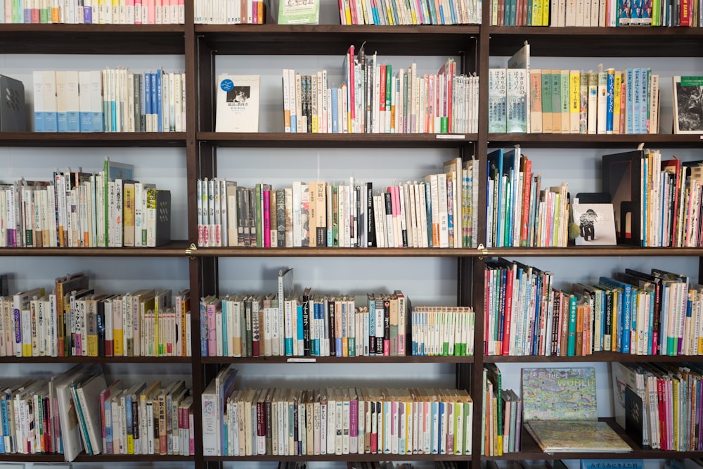 assorted books on brown wooden shelf at daytime