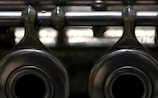 A close-up view of metallic mechanical components with a shiny, reflective surface, featuring two large circular openings and a horizontal rod extending across the top. The image has a slightly blurred background, highlighting the texture and material of the metal.