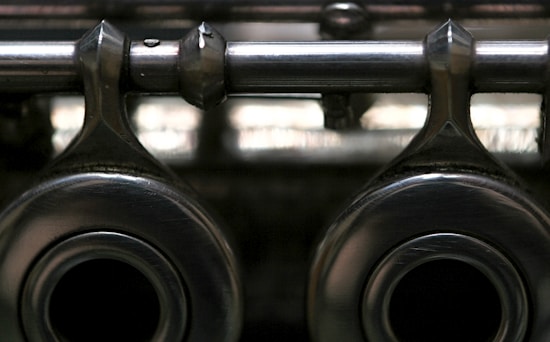 A close-up view of metallic mechanical components with a shiny, reflective surface, featuring two large circular openings and a horizontal rod extending across the top. The image has a slightly blurred background, highlighting the texture and material of the metal.