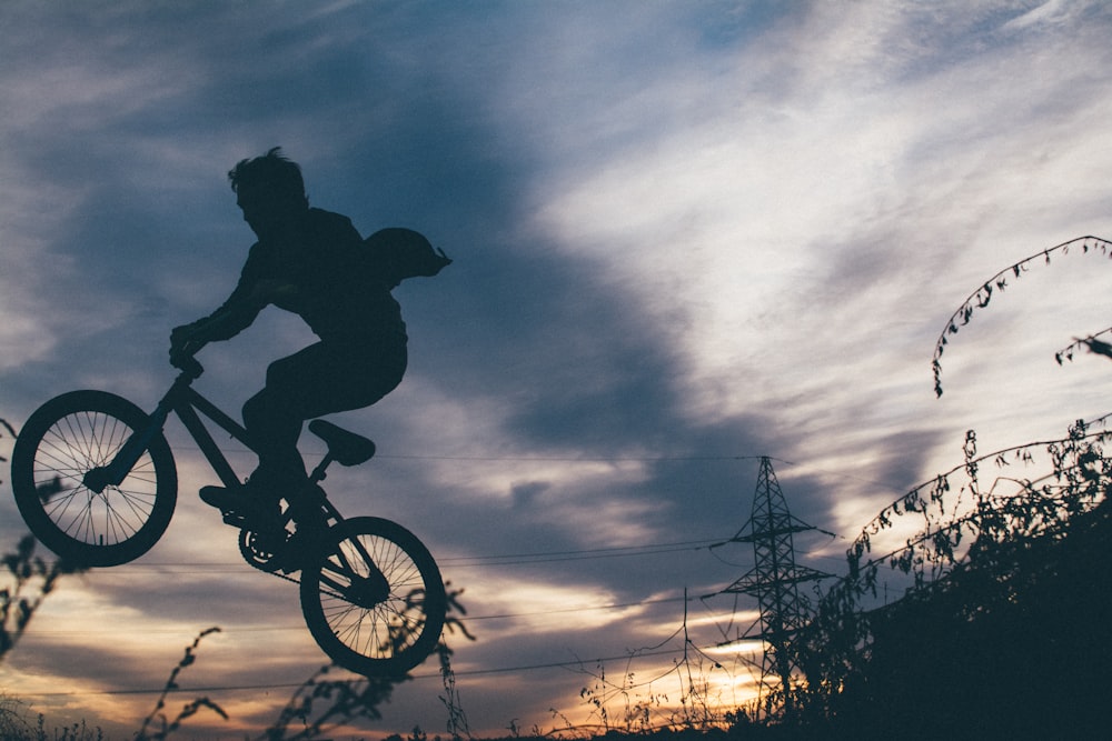 silhouette photo of bikers showing exhibition on air during orange sunset