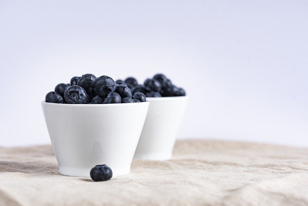 갈색 직물에 블루베리 과일 장소로 채워진 두 개의 흰색 세라믹 컵