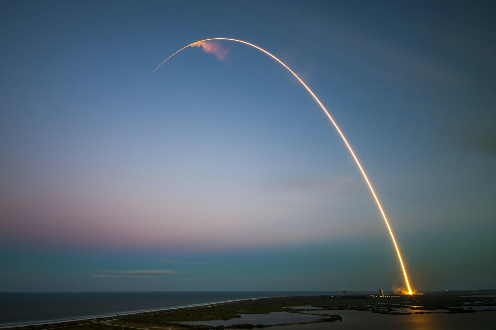 A rocket launch traces a bright arc through the dusk sky
