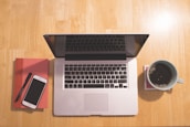 A modern office workspace with a smartphone, notebook, and coffee cup on a wooden desk.