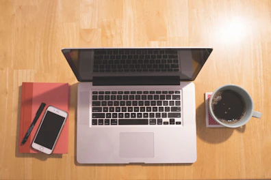 A modern tablet resting on a wooden desk next to a cup of coffee and notebook.