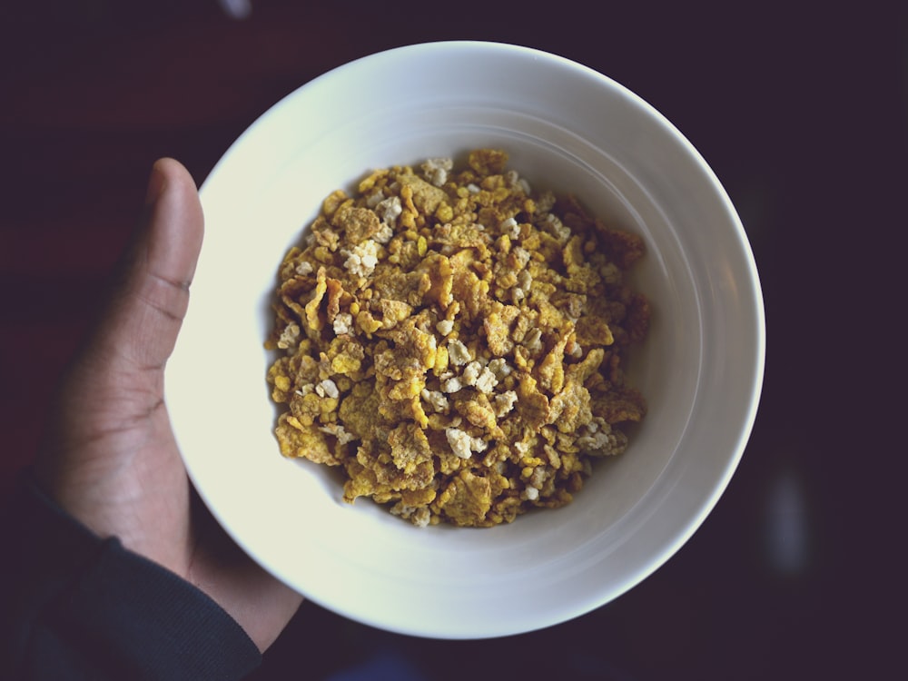 persona sosteniendo un cuenco de cerámica blanca lleno de cereal