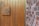 A wooden door with vertical panels is shown, featuring a large metal number 15 attached. Adjacent to the door is a red and brown brick wall.