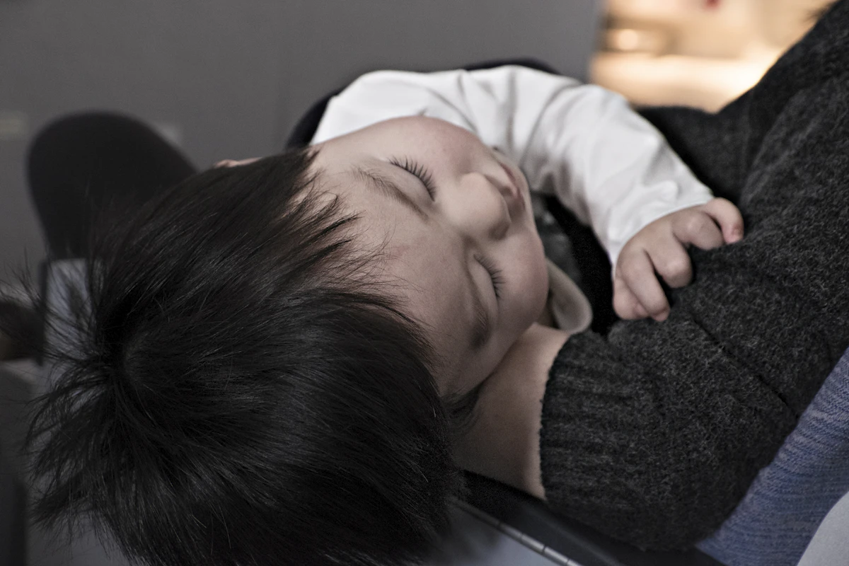 A toddler sleeping peacefully, nestled against a parent