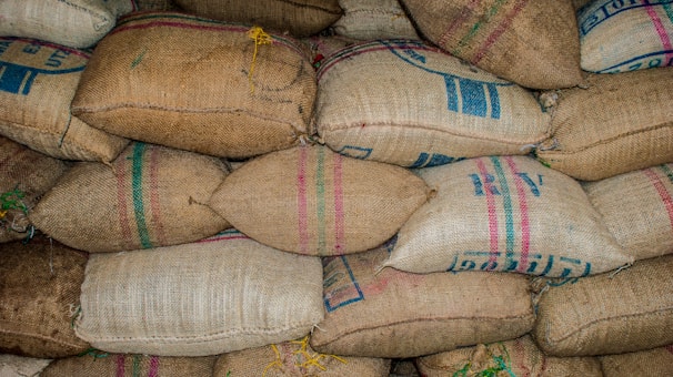 A stack of burlap sacks arranged in rows, some with colored stripes and printed text. The sacks are tightly packed and seem to be filled with granular material.