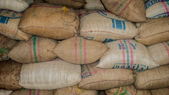 Stacks of heavy-duty jumbo bags filled with raw coconut shell charcoal ready for maritime shipment at a busy port.
