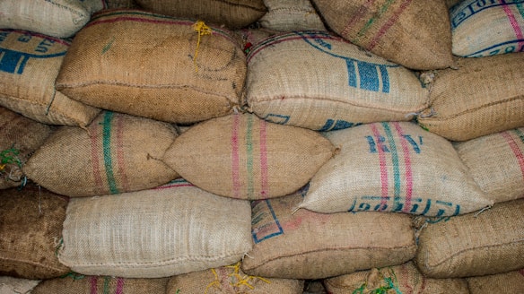 A stack of burlap sacks arranged in rows, some with colored stripes and printed text. The sacks are tightly packed and seem to be filled with granular material.