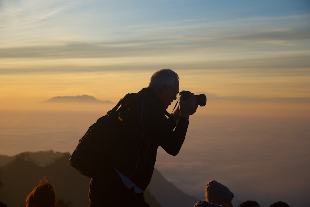 A silhouette of a man taking a photo while on top of a mountain