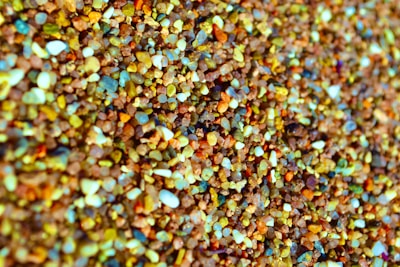 A close-up view of various small, colorful pebbles and grains of sand with different shapes and textures. The image captures the intricate details and the vibrant mixture of colors ranging from browns and blues to yellows and whites.