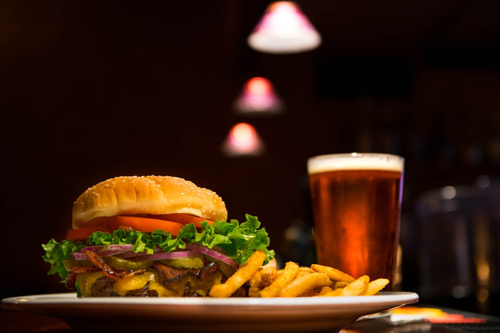Fotografia mostra um hambúrguer junto a uma porção de batatas fritas e, no segundo plano, um copo de cerveja. Foto: Edward Franklin | Unsplash.