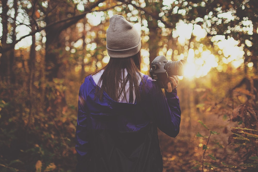 donna nella foresta che tiene la fotocamera DSLR durante l'ora d'oro