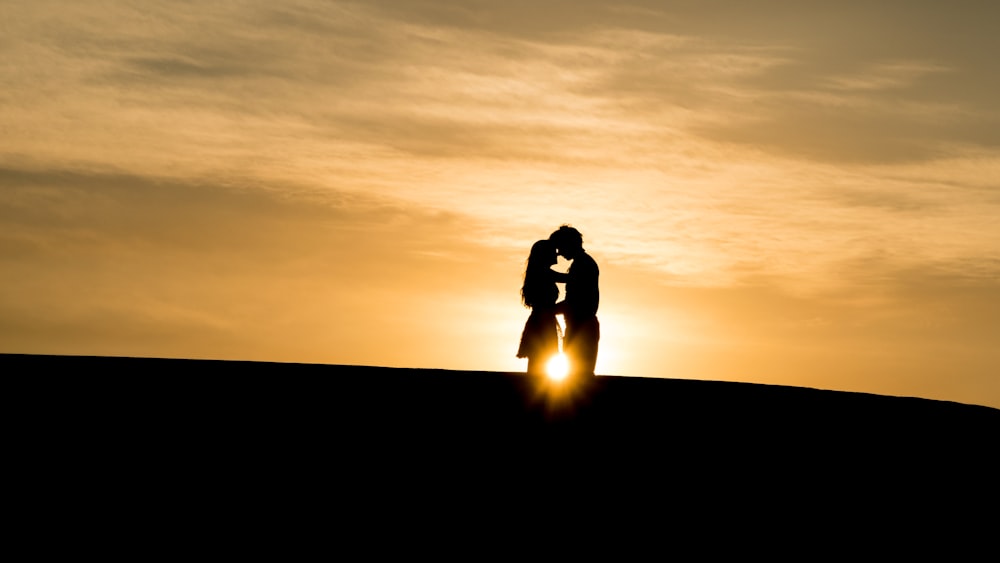 man and woman's silhouette on hill during golden hour