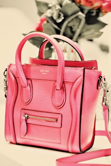 A sleek, gently worn pink leather handbag resting on a soft white surface with subtle pink accents.