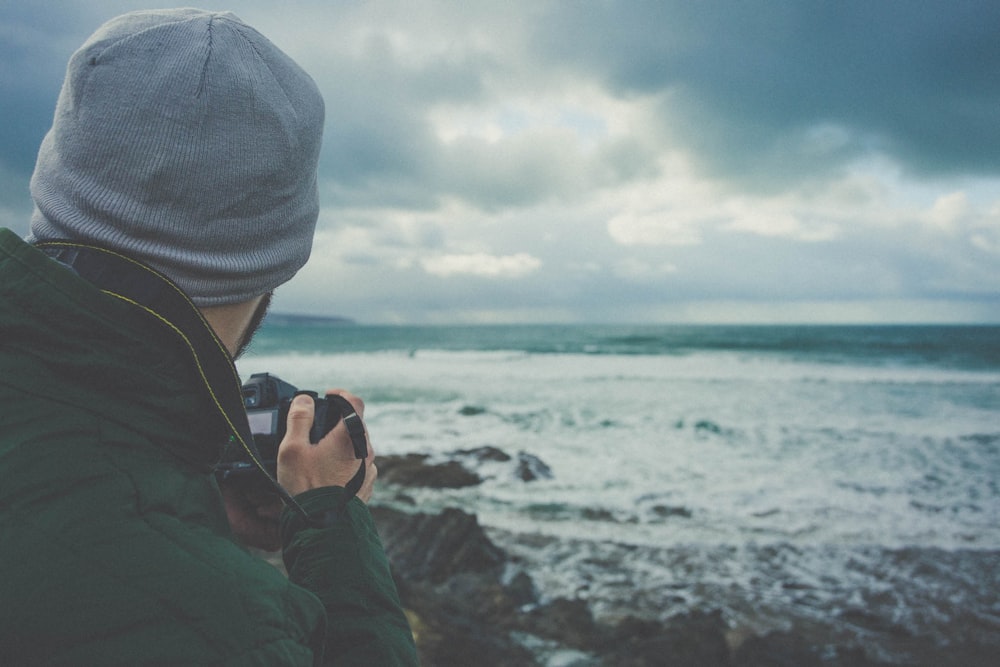 hombre sosteniendo una cámara DSLR tomando fotos de las olas de la playa