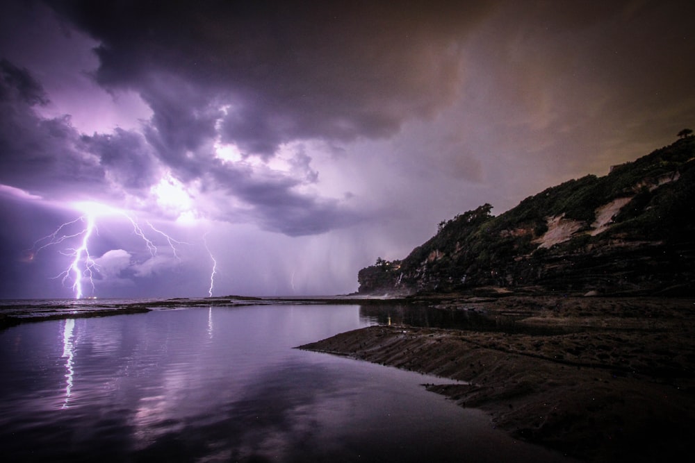 lightning near body of water and rock formation