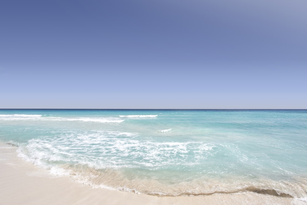 L’océan bleu clair se lave sur le rivage sablonneux par temps clair à Cancún