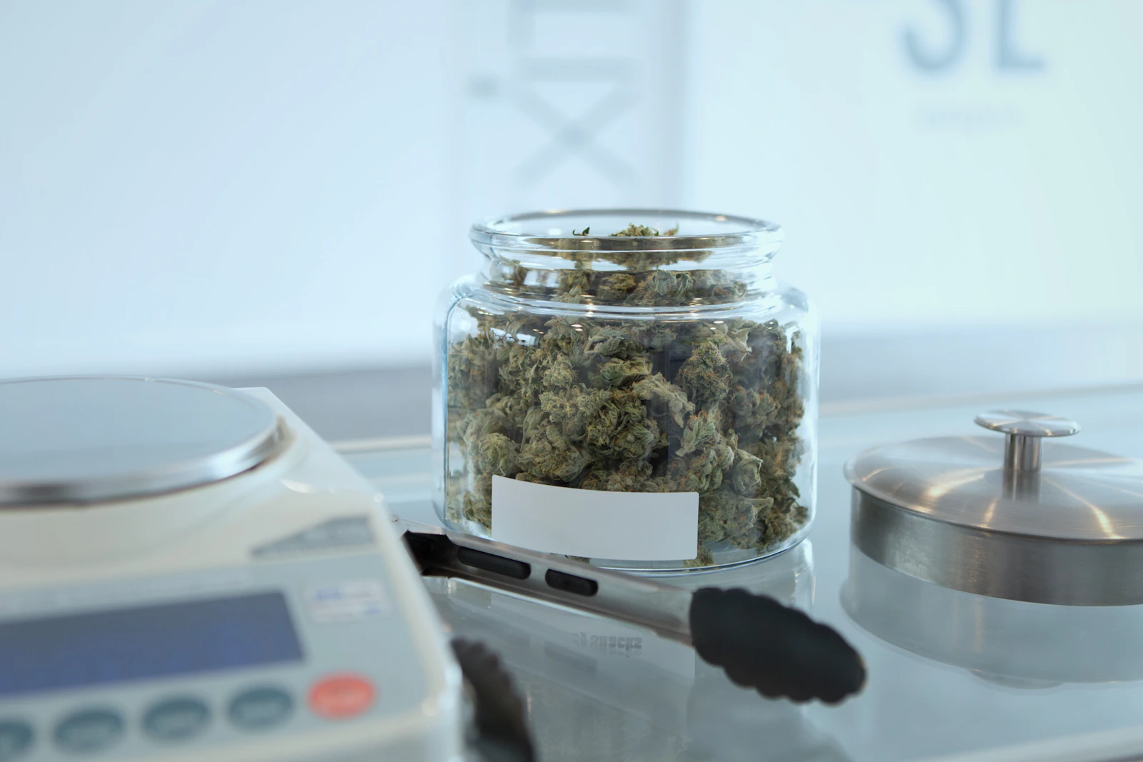 Cannabis flower in a glass jar beside a scale, representing gram-level inventory tracking in a licensed dispensary