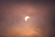Close-up of hands holding eclipse glasses with the sun partially covered in the background.