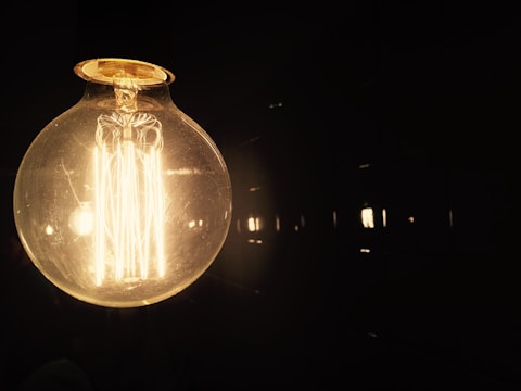 Close-up of a minimalist smart bulb glowing softly against a dark slate background.
