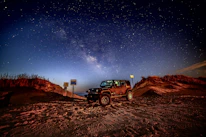 A luxury 4x4 vehicle parked near the dunes of the Sahara Desert under a starry night.