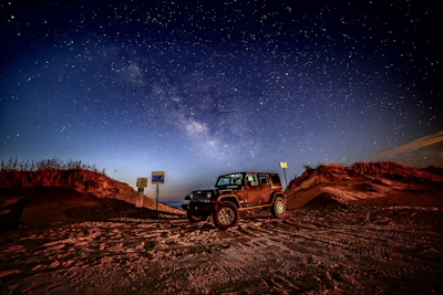 A luxury 4x4 vehicle parked near the dunes of the Sahara Desert under a starry night.