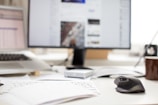 Close-up of hands typing on a laptop keyboard with scattered office documents around.